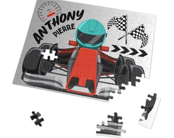 Op de afbeelding: Een grijze puzzel met een rode raceauto en een blauwe helm. De puzzel is gedeeltelijk in elkaar gezet en toont de naam "ANTHONY PIERRE" bovenaan. De raceauto heeft een geblokte vlag en een snelheidsmeter met het nummer 180.