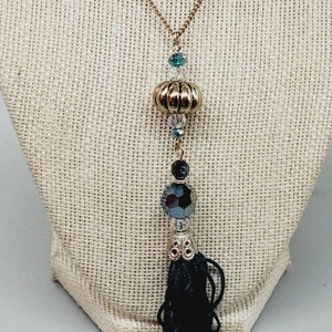 May include: A gold chain necklace with a black tassel and blue and clear crystal beads.