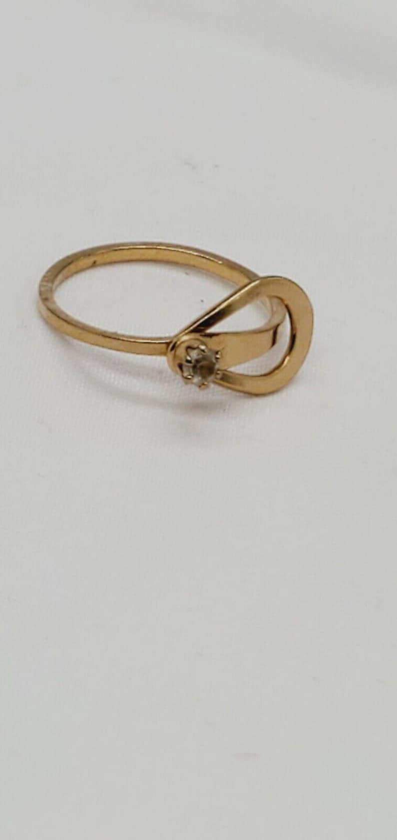 May include: A gold ring with a single clear stone set in the center of the band. The band is a simple, thin band with a unique design that wraps around the finger.