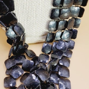 May include: A black necklace made of faceted square beads. The beads are strung together in a staggered pattern, creating a unique and eye-catching design.