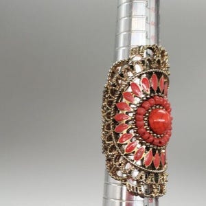 May include: A gold ring with a large red and gold floral design. The ring is on a ring sizer and the size is 6.5.