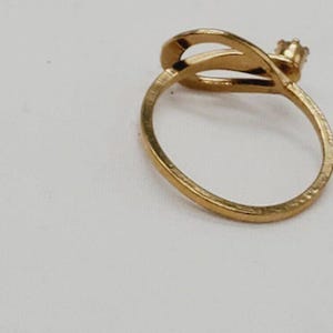May include: A gold ring with a unique design featuring a curved band and a small, clear stone.