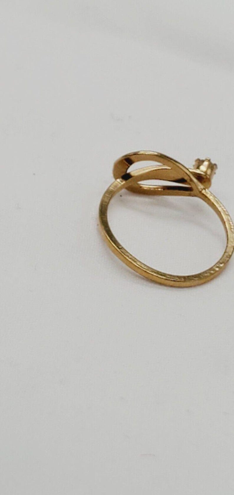 May include: A gold ring with a unique design featuring a curved band and a small, clear stone.