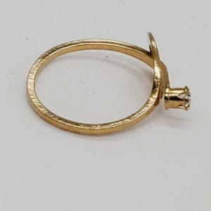 May include: A gold ring with a single diamond set in a prong setting. The ring is simple and elegant.