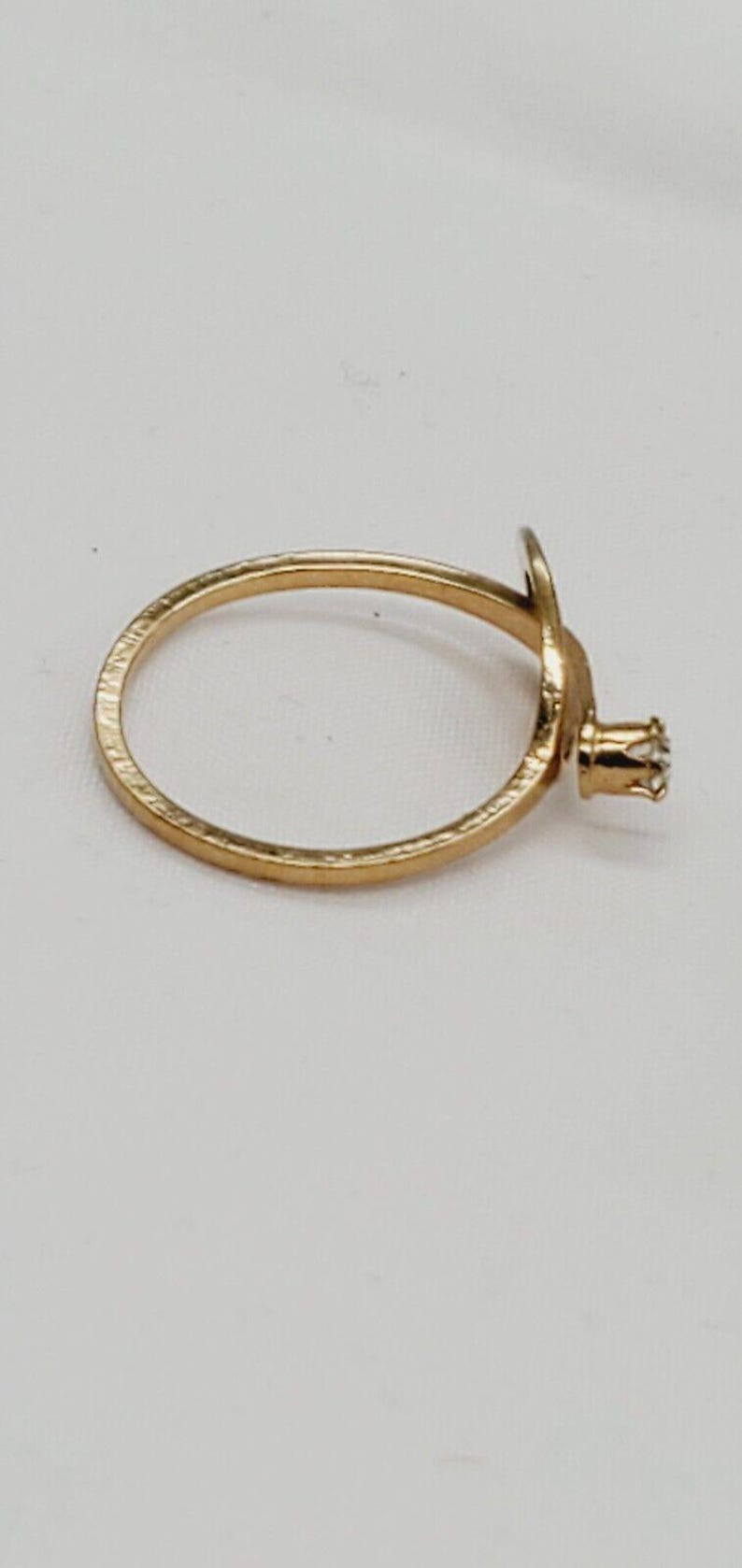 May include: A gold ring with a single diamond set in a prong setting. The ring is simple and elegant.