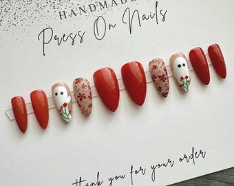 May include: Handmade press-on nails with a fall-themed design. The nails are red with a white ghost and floral pattern. The text "Handmade Press On Nails" and "Thank you for your order" are visible on the card.