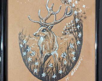 May include: A framed pen and ink drawing of a deer with large antlers, standing in a field of grass and white flowers. The artwork is set against a tan background and signed by the artist.