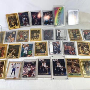 May include: A collection of twenty-six rectangular basketball trading cards featuring Shaquille O'Neal in various game action poses and team uniforms. Each card is individually encased in a clear plastic protective sleeve or a hard plastic holder.