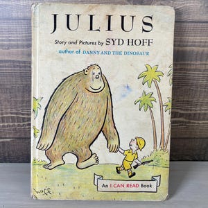 Puede incluir: Libro infantil vintage "JULIUS" de Syd Hoff. La portada muestra un oso grande y amigable caminando con un niño pequeño. El libro tiene palmeras de fondo y el texto "An I CAN READ Book".