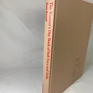 May include: The Woman's Day Book of Soft Toys and Dolls by Joan Russell. A tan hardback book with red text on the spine.