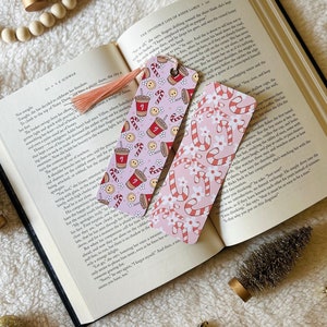 May include: Two pink and white Christmas themed bookmarks. One bookmark features a red coffee cup with a candy cane and snowflakes. The other bookmark features red and white candy canes with white snowflakes.