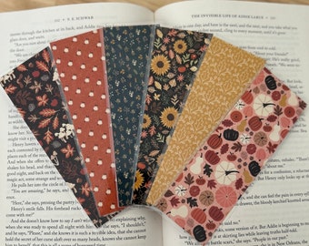 May include: Six colorful bookmarks with fall-themed designs. The bookmarks feature various patterns of leaves, pumpkins, sunflowers, and other autumnal elements. The bookmarks are arranged in a row, with the top of each bookmark visible.
