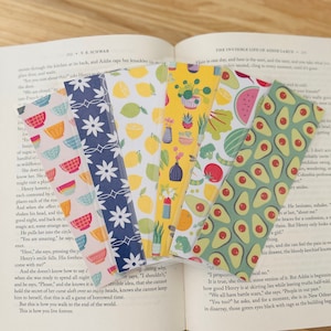 May include: A set of ten colorful bookmarks featuring various designs, including lemons, avocados, and potted plants. The bookmarks are made of a clear plastic material with a printed design.