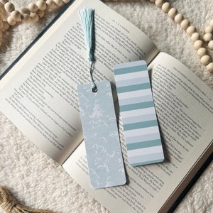 May include: Two bookmarks with a blue and white striped pattern and a blue and white wave pattern. The bookmarks are on top of an open book with a white background.