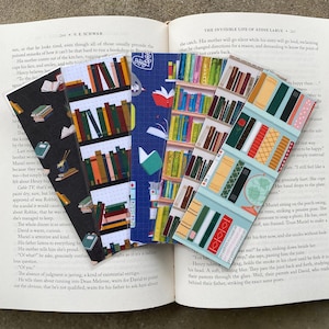 May include: Set of five colorful bookmarks featuring illustrations of bookshelves filled with books. The bookmarks are printed on a blue, green, and red background.