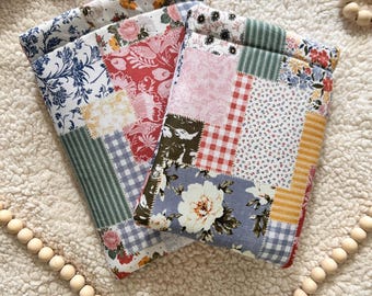 May include: Two rectangular fabric pouches featuring a patchwork design of various floral, gingham, and striped patterns in shades of red, blue, green, yellow, and white. The pouches are constructed from multiple quilted fabric squares.
