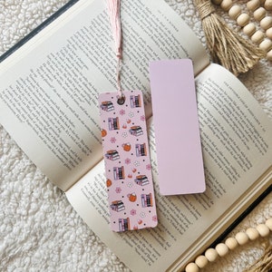 May include: A pink and orange bookmark with a pattern of stacked books, teacups, and candy corn. The bookmark has a tassel on the top.