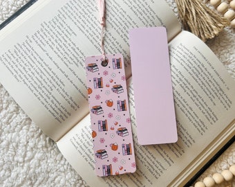 May include: A pink and orange bookmark with a pattern of stacked books, teacups, and candy corn. The bookmark has a tassel on the top.