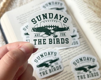 May include: White sticker with green text and a football and eagle graphic. The text reads "SUNDAYS ARE FOR THE BIRDS". Several stickers are visible, some on an open book.