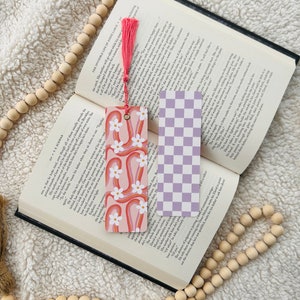 May include: Two bookmarks, one with a pink and orange rainbow design with white flowers and the other with a checkered pattern in shades of purple and white.
