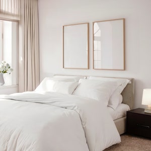 May include: A white bed with a white duvet cover and pillows, a beige headboard, and two framed pictures on the wall above the bed.