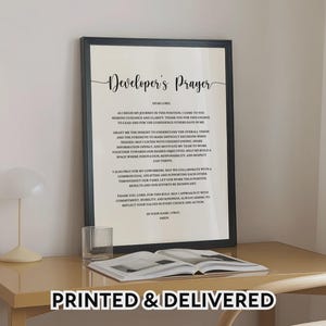 May include: A framed wall art print titled Developer's Prayer in black text on a cream background. The text includes a prayer for guidance, insight, and collaboration in a professional setting. The frame is black and rectangular in shape.