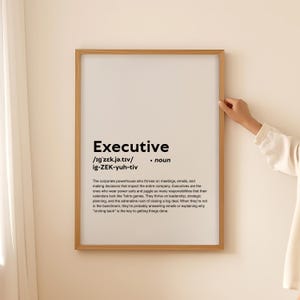 May include: A black and white printable poster with the definition of the word "Executive". The poster is framed in a light brown frame and is hanging on a white wall.