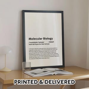 May include: A framed print with the words "Molecular Biology" in a black frame. The print includes a definition and a humorous description of molecular biology. The text is in black on a cream background. The print is on a desk with a book and a glass.