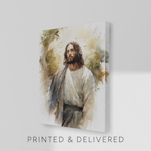 May include: A rectangular canvas print featuring a watercolor-style illustration of a man with long brown hair and a beard, wearing a white robe and a dark wrap. The figure is positioned amidst soft, muted green and brown foliage. Text reads PRINTED & DELIVERED.