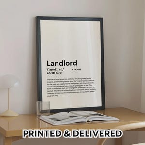 May include: A framed print with the definition of "Landlord" in black text on a white background. The print is displayed on a light brown desk with an open book and a glass. The words "PRINTED & DELIVERED" are at the bottom.