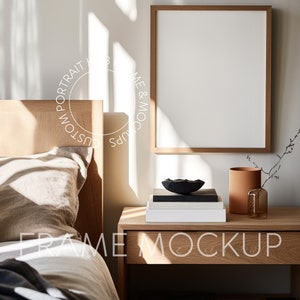 May include: A wooden frame mockup with a white background, sitting on a wooden nightstand with a book stack, a black bowl, and a brown vase. The frame is in a bedroom setting with a bed in the background.