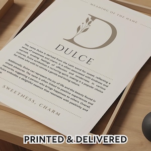 May include: A framed print featuring the name "Dulce" with a detailed explanation of its meaning. The design includes a decorative "D" and the text "PRINTED & DELIVERED" at the bottom, presented on a wooden surface.