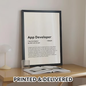 May include: A framed print with the text "App Developer" and a definition. The print is in a black frame and sits on a light-coloured desk. A glass and an open book are also on the desk. The text "PRINTED & DELIVERED" is at the bottom.