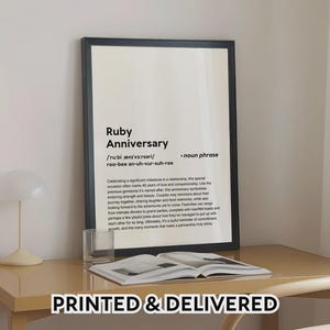 May include: A framed print with the words "Ruby Anniversary" in black text. The print is on a desk with a glass and an open book. The text at the bottom says "PRINTED & DELIVERED".