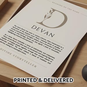 Puede incluir: Una impresión enmarcada con el nombre "DEVAN" en una fuente estilizada, con una "D" decorativa y texto que describe los orígenes y el significado del nombre. La impresión incluye el texto "PRINTED & DELIVERED" en la parte inferior y se muestra en una bandeja de madera.