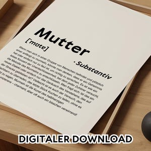 May include: A white print with the German word "Mutter" in bold black letters, meaning "mother". The print includes a definition and the text "DIGITALER DOWNLOAD". The print is in a wooden frame.