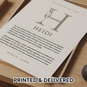 May include: A framed print featuring the name "Heidi" in a stylish font, with a decorative "H" and botanical accents. The print includes a description of the name's origins and meaning, emphasizing qualities like kindness and joy. The words "Printed & Delivered" are at the bottom.