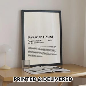 Pode incluir: Uma impressão emoldurada em preto com o texto "Bulgarian Hound" e sua definição. A impressão está em uma mesa com uma lâmpada, um copo e um livro aberto. As palavras "PRINTED & DELIVERED" estão na parte inferior.