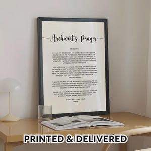 May include: A framed wall art print featuring the Archivist's Prayer in black text on a cream background. The text includes a title and a multi-paragraph prayer addressed to the Lord, focusing on the preservation of records and historical artefacts.