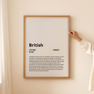May include: A framed print featuring the word "British" and its phonetic pronunciation. The text below humorously defines a British person, describing their love for tea, debates, and bowler hats. The frame is light brown.