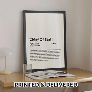 Puede incluir: Impresión enmarcada en negro con el texto "Chief Of Staff" y una definición. La impresión incluye una descripción del rol. La frase "PRINTED & DELIVERED" está en la parte inferior. El marco está sobre un escritorio marrón claro.
