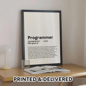 Peut inclure: Un cadre noir avec la définition de "Programmeur" en texte noir sur fond blanc. L'impression est sur un bureau brun clair avec un verre et un livre ouvert. Le texte "PRINTED & DELIVERED" est en bas.
