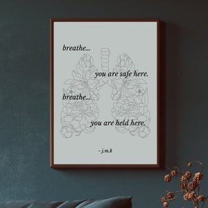 May include: A black and white line drawing of lungs with flowers inside. The text "breathe... you are safe here. breathe... you are held here. - j.m.k" is printed below the image. The image is framed and hanging on a dark blue wall. The text "JOSH KISZKA GVF MEDITATION POSTER" is printed below the image.