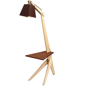 K&ouml;nnte beinhalten: Eine Stehlampe aus Holz mit einem braunen Stoffschirm und einem kleinen Regal. Die Lampe hat ein einzigartiges Design mit einem langen, abgewinkelten Arm und einem dreieckigen Sockel.