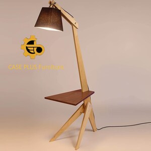 K&ouml;nnte beinhalten: Eine Stehlampe aus Holz mit einem schwarzen Stoffschirm und einem kleinen Regal. Die Lampe ist aus hellem Holz gefertigt und hat ein modernes Design. Die Lampe steht auf einem wei&szlig;en Hintergrund. CASE PLUS Furniture.