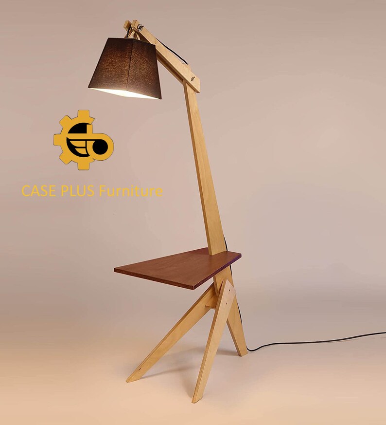 K&ouml;nnte beinhalten: Eine Stehlampe aus Holz mit einem schwarzen Stoffschirm und einem kleinen Regal. Die Lampe ist aus hellem Holz gefertigt und hat ein modernes Design. Die Lampe steht auf einem wei&szlig;en Hintergrund. CASE PLUS Furniture.
