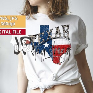 May include: A white t-shirt with a graphic of the state of Texas in the shape of a flag with the words "Texas Stay Strong" printed on it. The Texas flag graphic has a leopard print border.