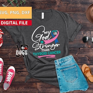 May include: A gray t-shirt with the text "My God is Stronger Than Thyroid Cancer" in white. A pink ribbon with a blue ribbon inside is in the shape of a heart.