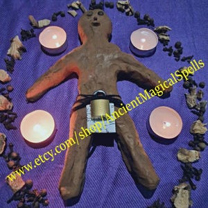 May include: A brown clay figure with a padlock, surrounded by candles, herbs, and spices on a purple cloth. The text "www.etsy.com/shop/AncientMagicalSpells" is visible.