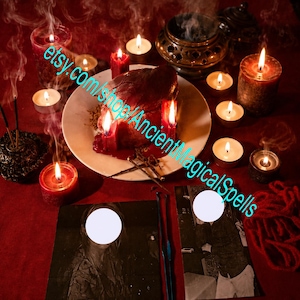 May include: A ritualistic arrangement on a red surface featuring a central white plate with a dark, heart-shaped object, surrounded by multiple lit red and white candles, incense smoke, a metal burner, and two black and white photographs with white circles.